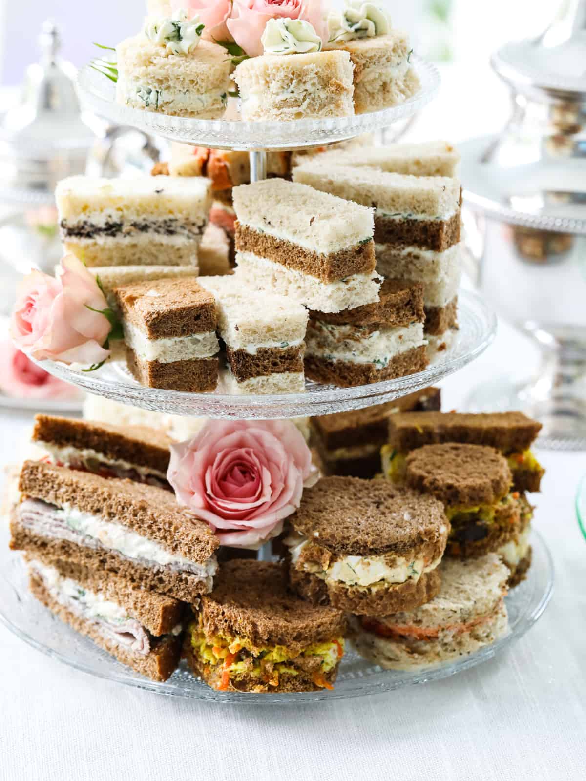 Layered tea sandwiches and ones filled with curry chicken and egg salad on a fancy tray. 
