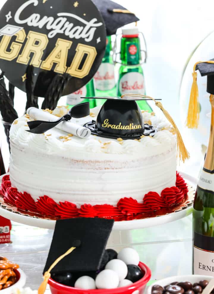 A grad party with red, white, and black food themed items on a table like a cake and snacks.