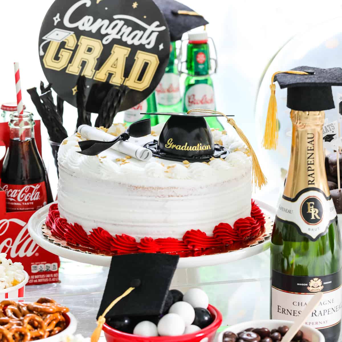 A grad party with red, white, and black food themed items on a table like a cake and snacks.