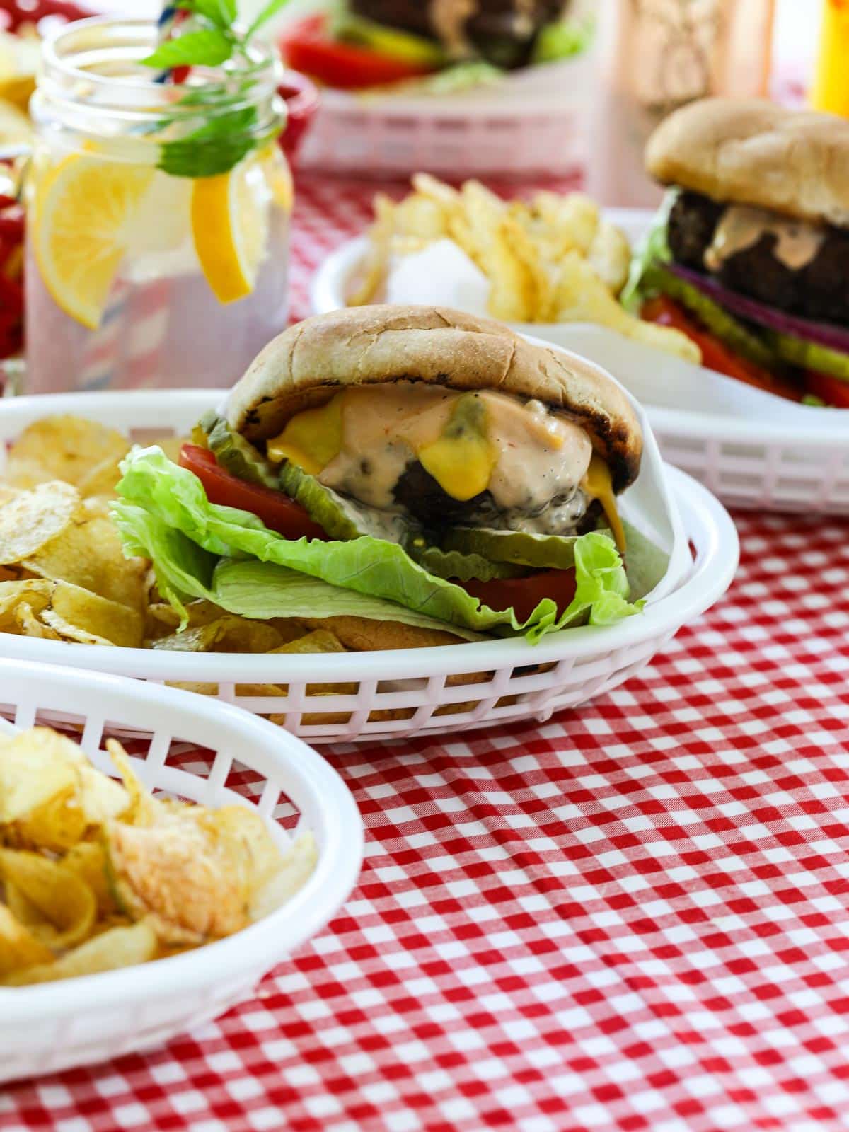 A cooked hamburger in a white basket with potato chips at a cookout. 