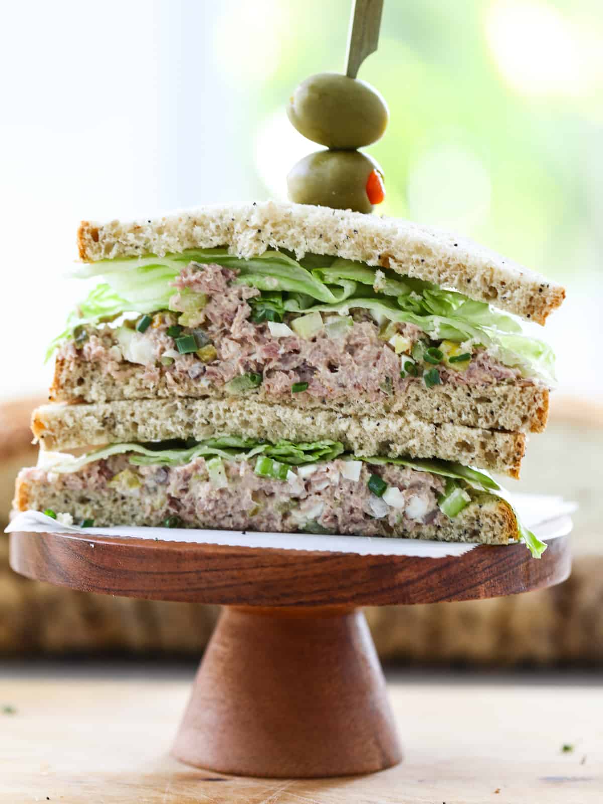 Ham salad on a sandwich sliced in half with an olive garnish. 