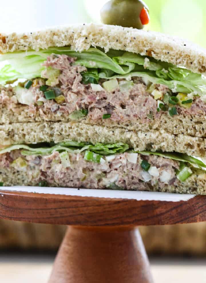 A ham salad sandwich sliced in half, stacked on a wood pedestal with crisp lettuce.