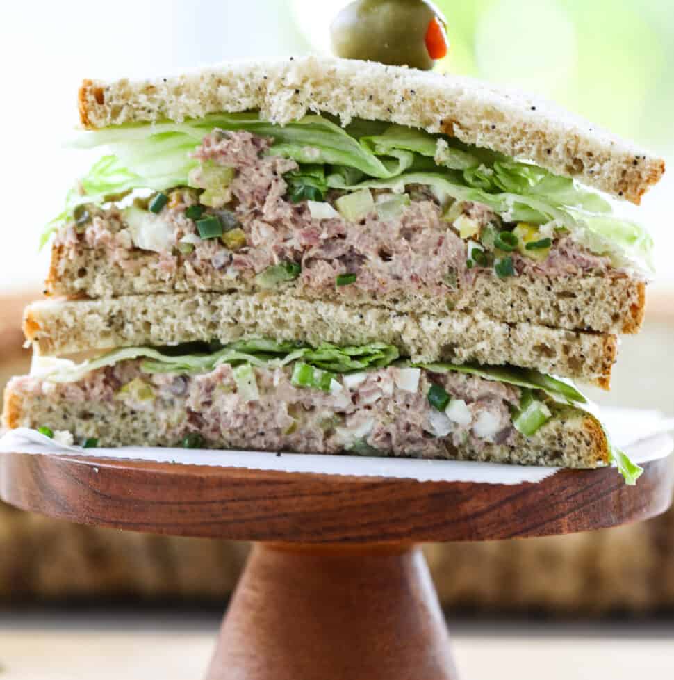 A ham salad sandwich sliced in half, stacked on a wood pedestal with crisp lettuce.