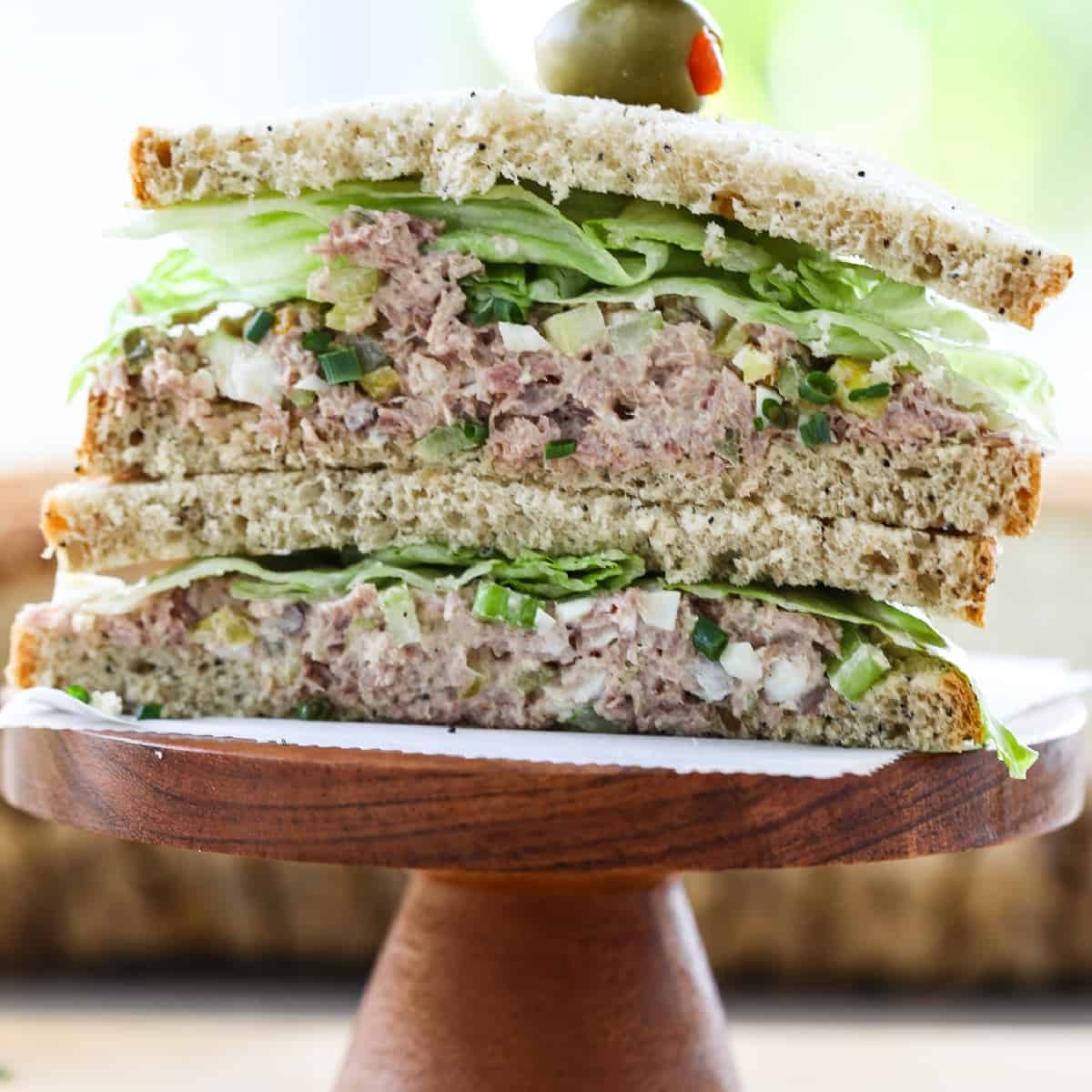 A ham salad sandwich sliced in half, stacked on a wood pedestal with crisp lettuce.