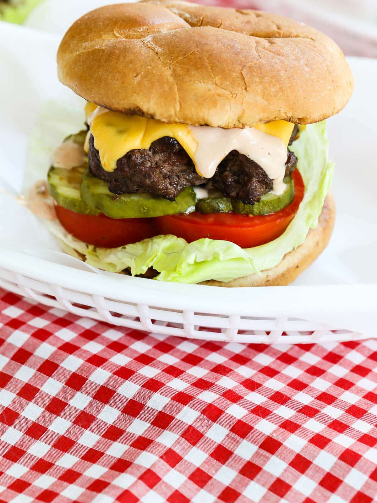 A grilled hamburger in a white food basket with cheese, lettuce, and tomato.