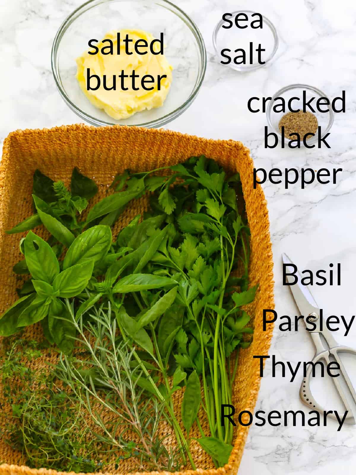 All the ingredients labeled to make herb butter including fresh herbs, butter, salt and pepper.