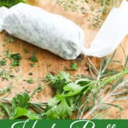 Herb butter wrapped in parchment paper on a cutting board with chopped herbs.