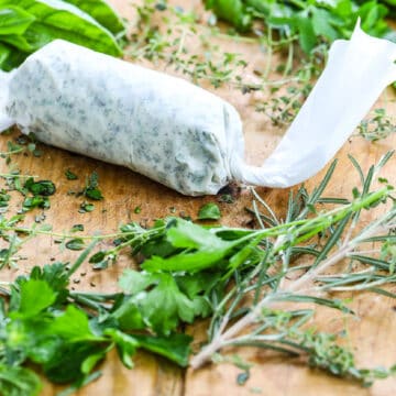 Homemade herb butter wrapped in parchment paper on a cutting board with fresh herbs.