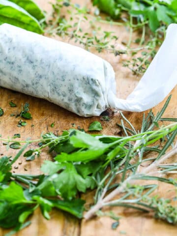 Homemade herb butter wrapped in parchment paper on a cutting board with fresh herbs.