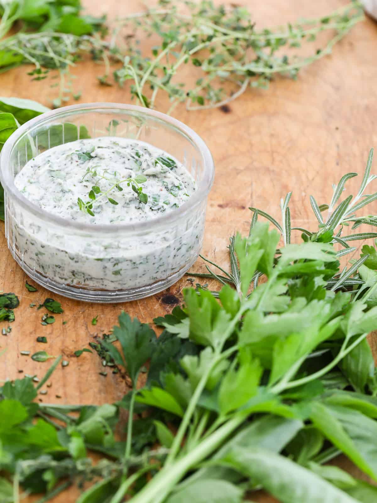 A clear round small dish filled with herb butter and herbs chopped on a cutting board.