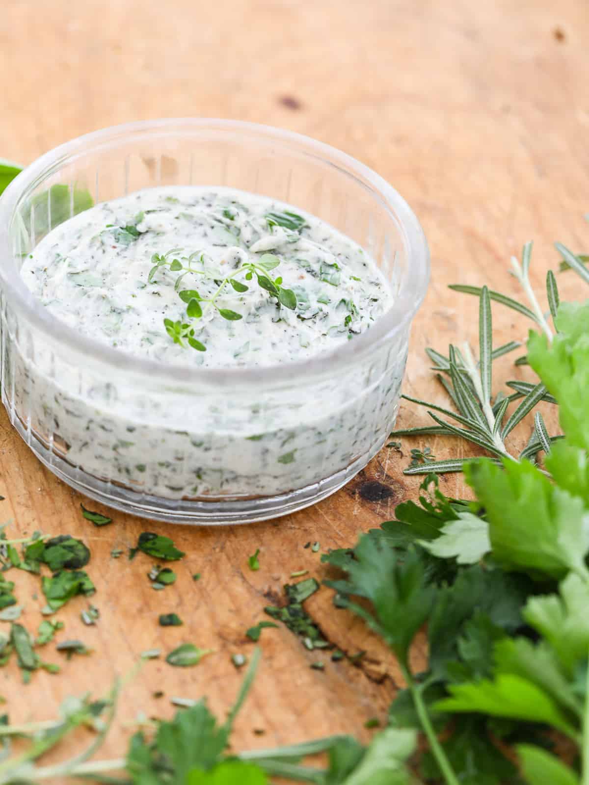 Cutting board with a small glass round dish filled with homemade herb butter.