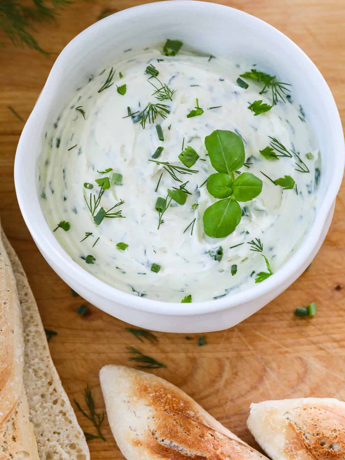 Close up of a white ceramic bowl filled with a white creamy herb dip garnished with fresh herbs.