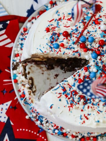 An ice cream cake with a slice removed and covered in colorful sprinkles.