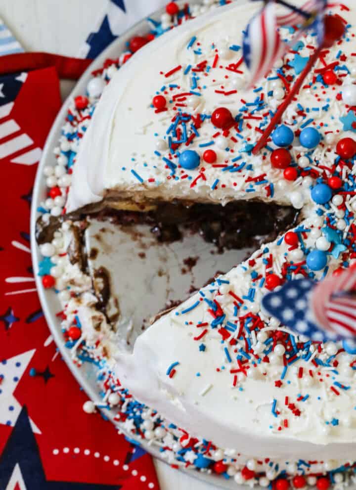 An ice cream cake with a slice removed and covered in colorful sprinkles.