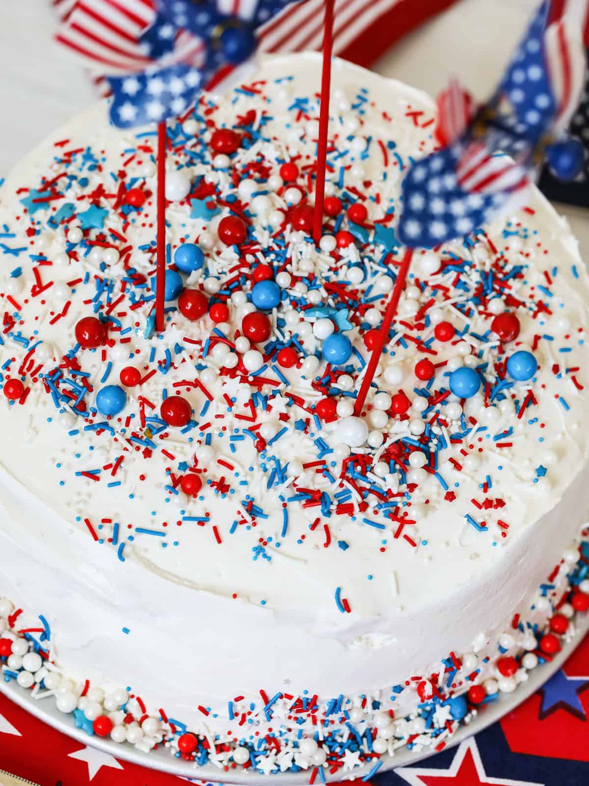 A white round ice cream cake with red white and blue sprinkles and pinwheels.
