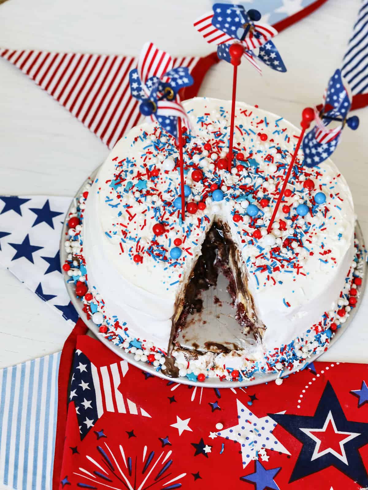 A round ice cream cake made at home with patriotic sprinkles and a slice removed. 