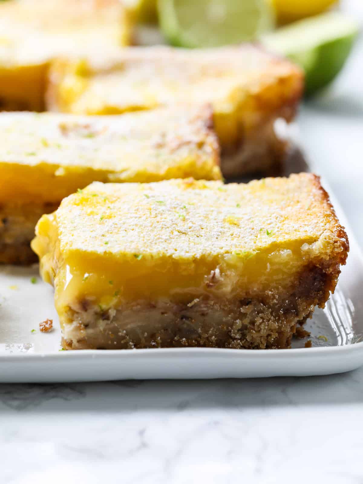 A large lemon bar sliced on a white plate with the filling dripping out. 