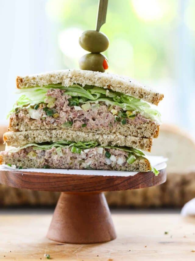 A ham salad sandwich sliced in half on a wood stand with an olive on top.