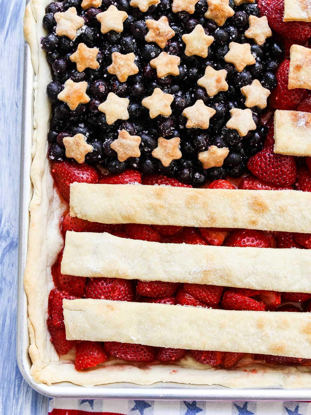 A close up view of a baked sheet pan pie shaped like an American Flag with strawberries and blueberries.