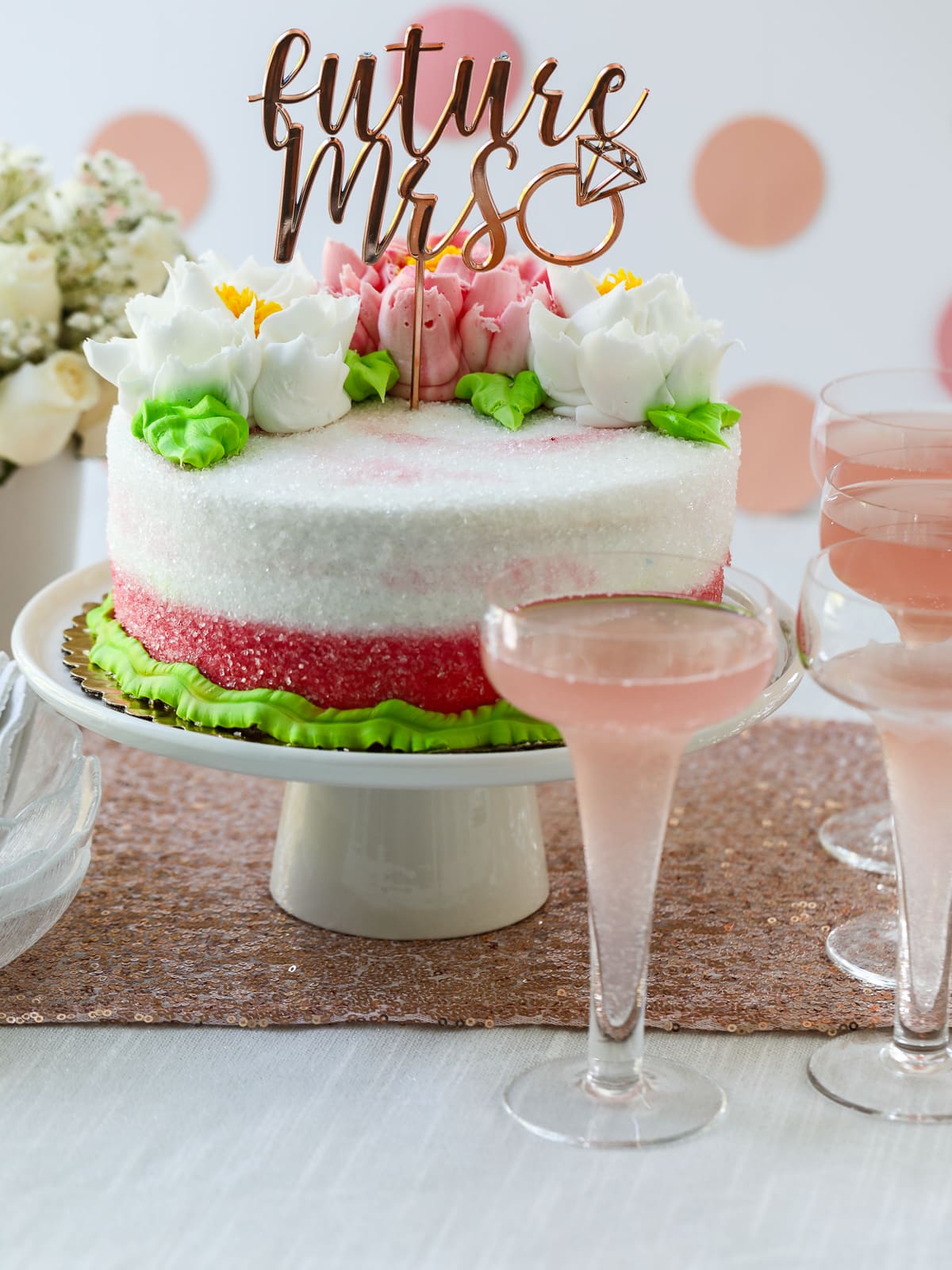 A pink and white cake decorated for a wedding shower with pink champagne. 