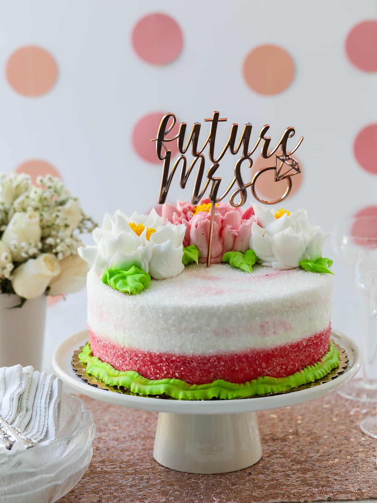 A bridal shower party with pink and white cake on a white cake stand, decorations, and glasses of pink champagne.