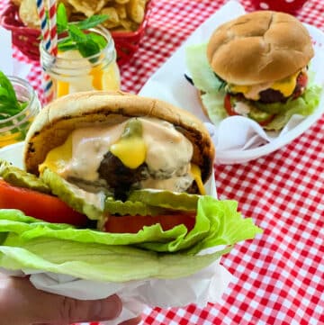 A grilled burger loaded with toppings and served at a cookout in paper lined plastic baskets.