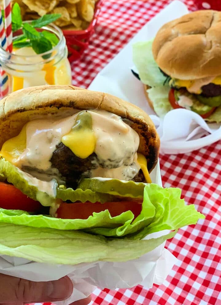 A grilled burger loaded with toppings and served at a cookout in paper lined plastic baskets.