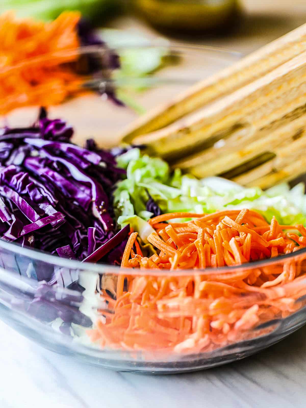 Carrots with purple and green cabbage shredded finely in a clear bowl to make coleslaw. 