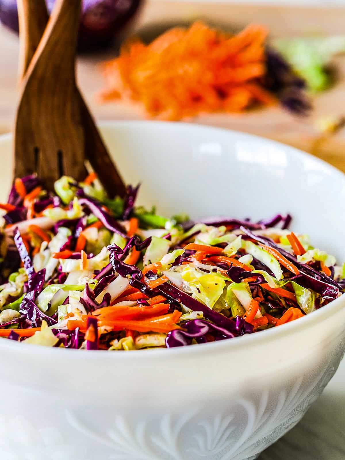 A white bowl filled with a tri color coleslaw recipe with wood salad tongs.