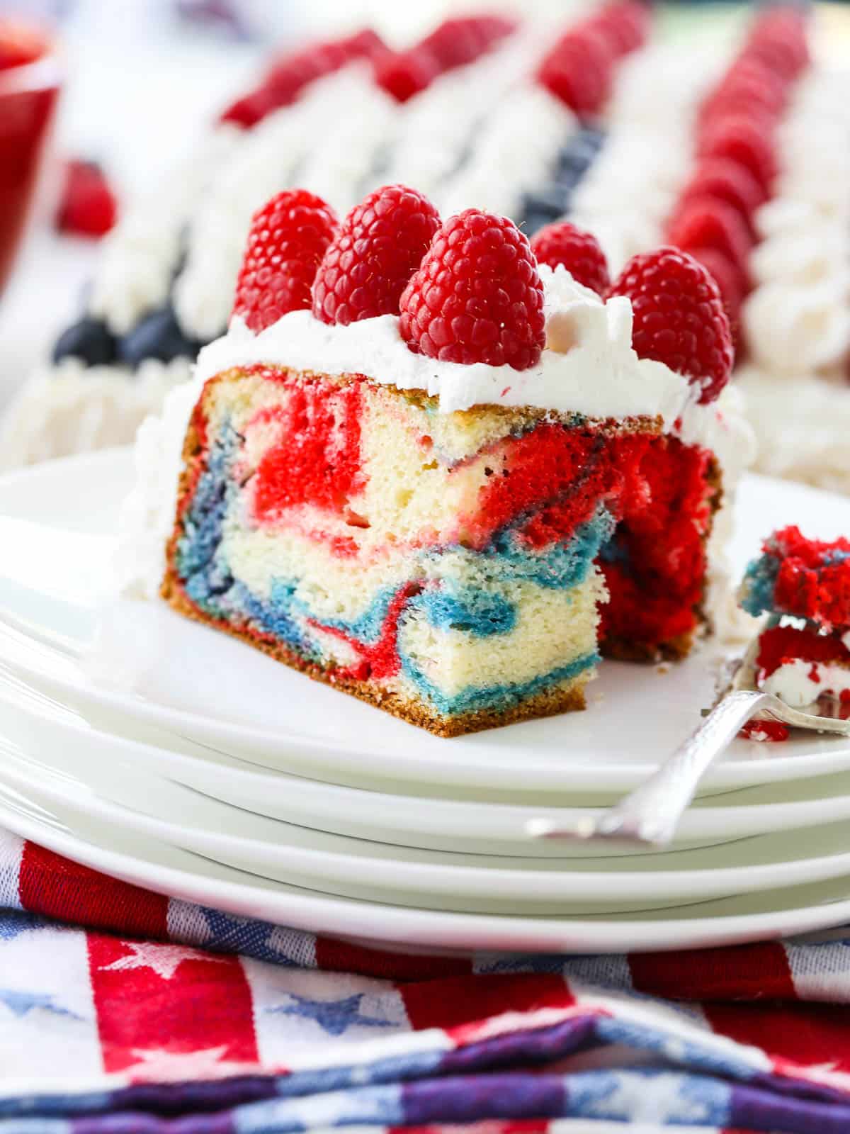 A slice of red, white and blue cake topped with white frosting and red berries. 