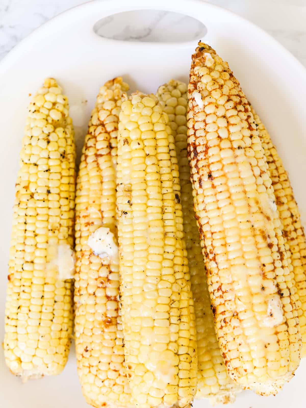 Seasoned butter grilled corn on a white platter.