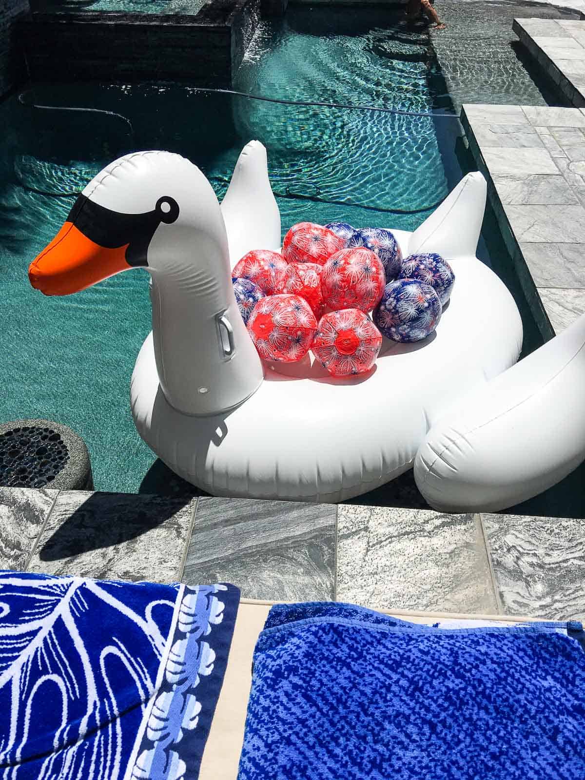 A white inflateable swan floating in a pool filled with red and blue July 4th beach balls. 