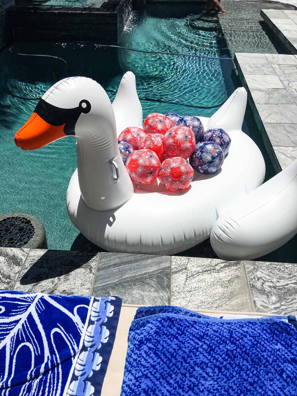 A white inflateable swan floating in a pool filled with red and blue July 4th beach balls.