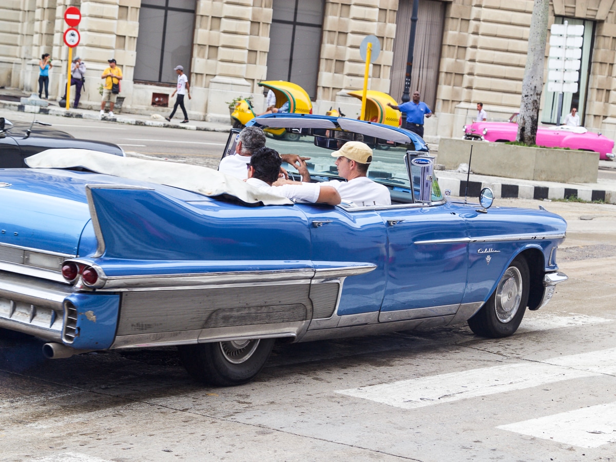 A blue convertible car in Cuba with people riding around Havana. 