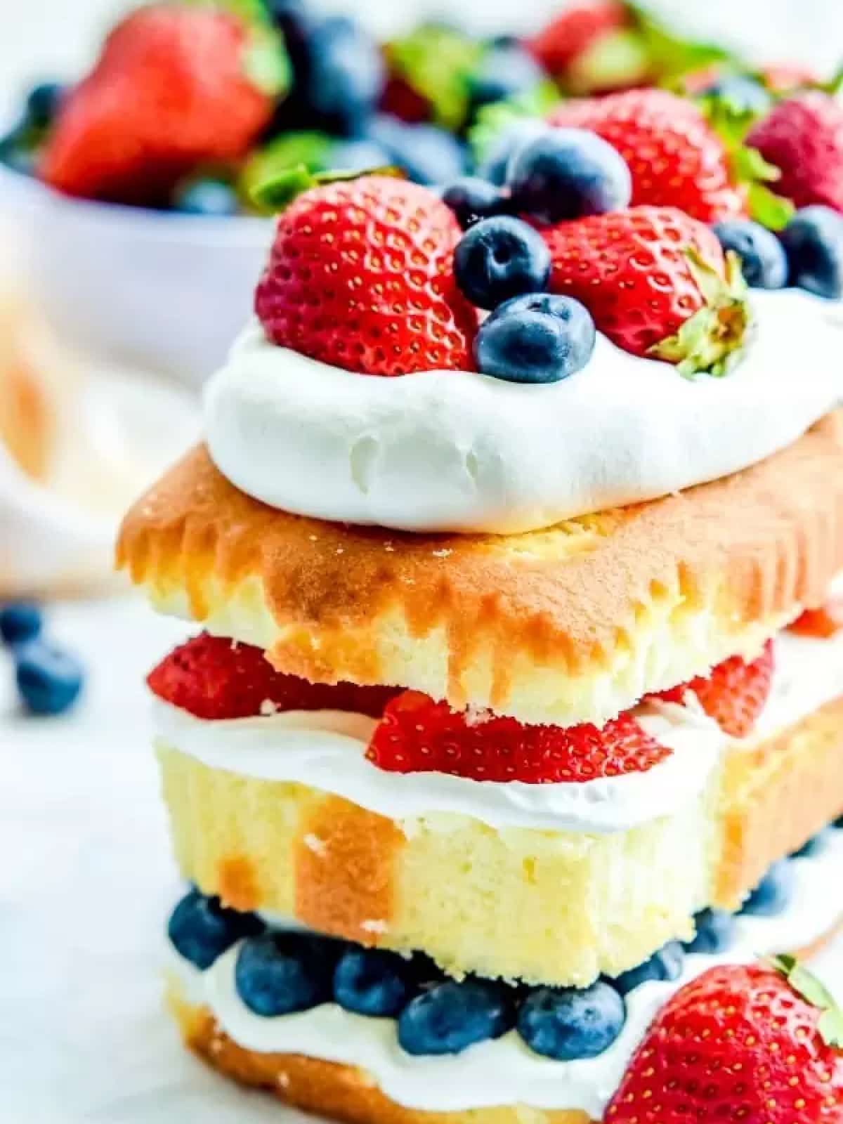 A layered pound cake with whip cream in between the layers and strawberries and blueberries on top.