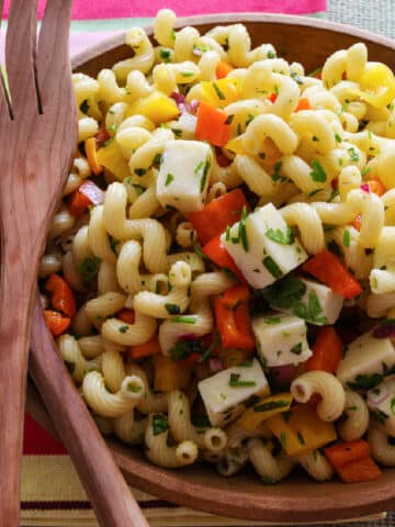 A wooden bowl filled with pasta salad and wooden serving tongs.