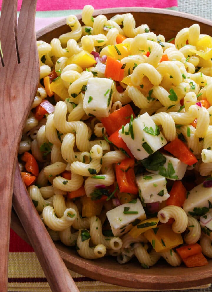 A wooden bowl filled with pasta salad and wooden serving tongs.