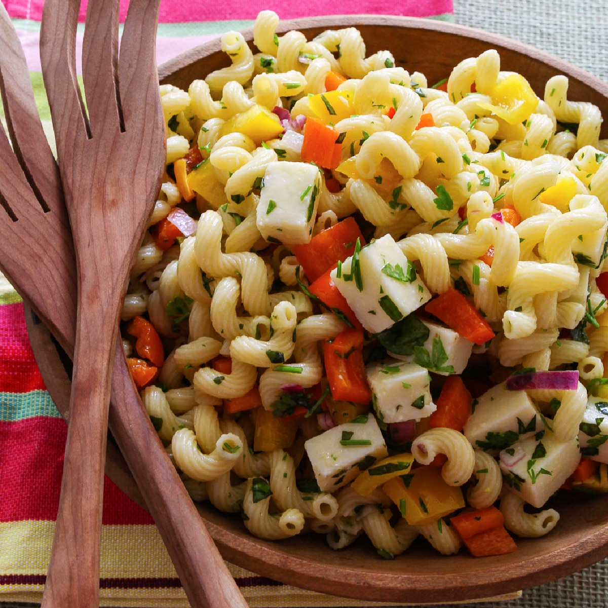 A wooden bowl filled with pasta salad and wooden serving tongs.