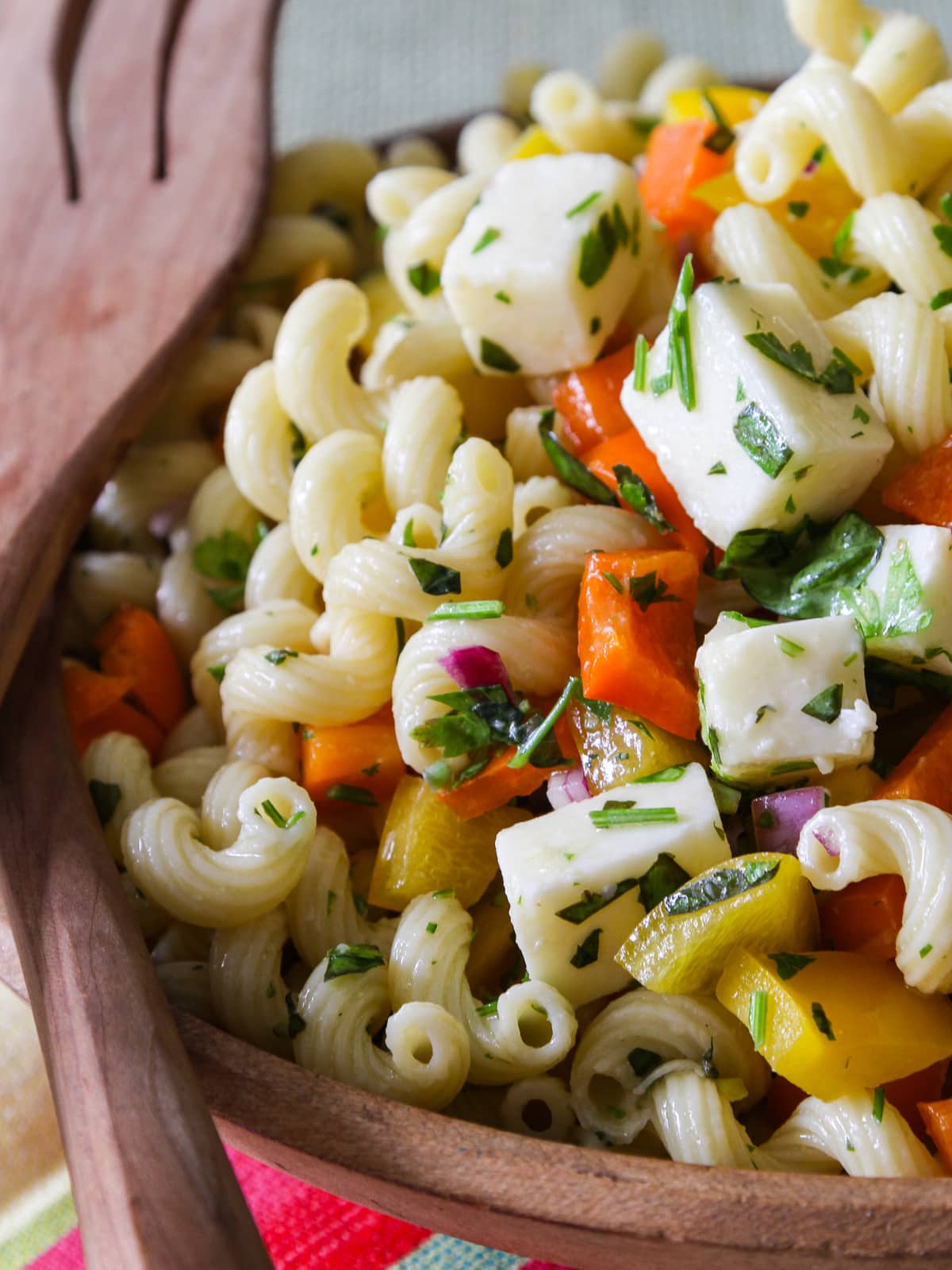 A wood bowl filled with pasta salad and fancy wooden serving tongs. 