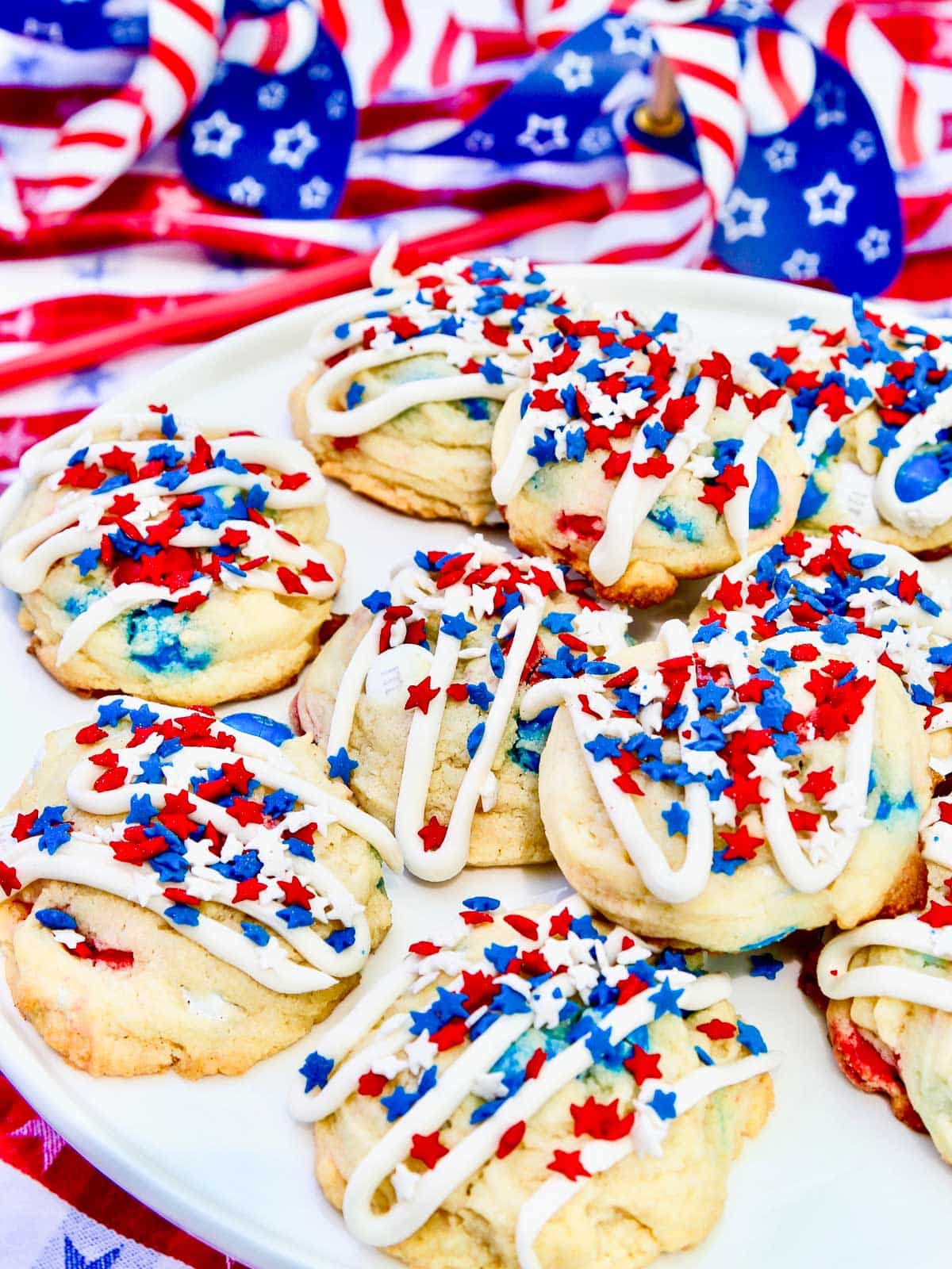 Patriotic red, white and blue cookies with sprinkles and a drizzle of white icing on a plate at a July 4th party. 