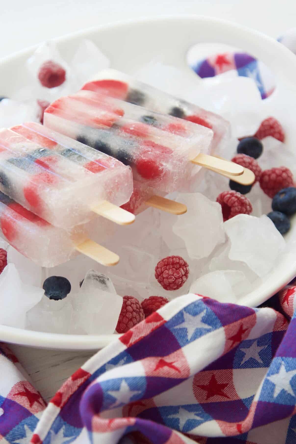 Frozen coconut water popsicles on a plate with berries and a July 4th towel. 