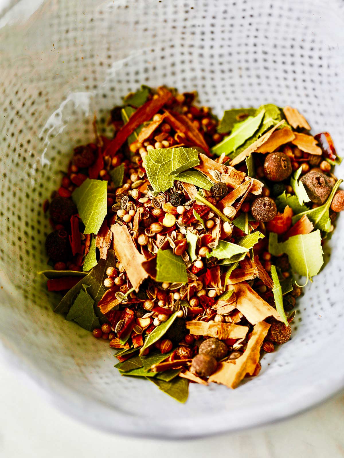 A white ceramic bowl filled with mixed pickling spice blend. 