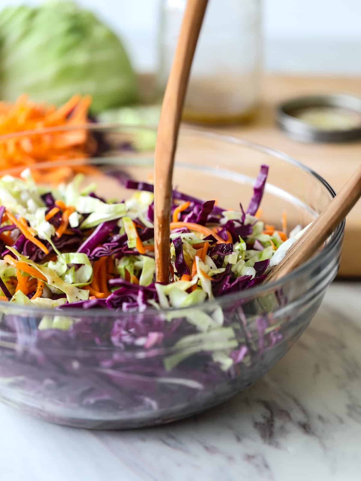 Coleslaw in a clear bowl with wood serving tongs.