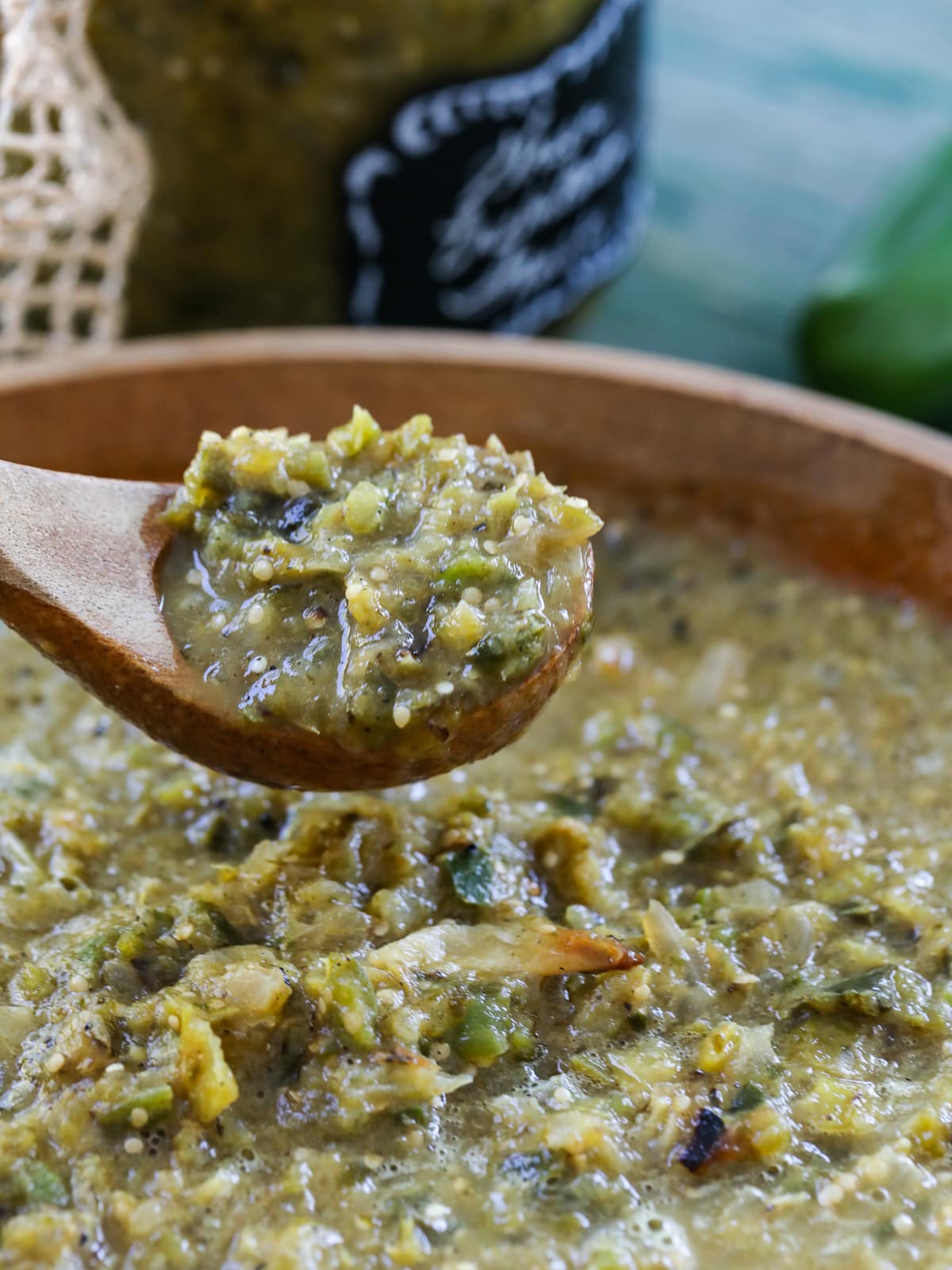 A wood spoon scooping out a spoonful of green enchilada sauce from a wood bowl of it. 