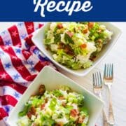 Looking down on to two white square bowls filled with potato salad on a red white and blue star towel and two silver forks.