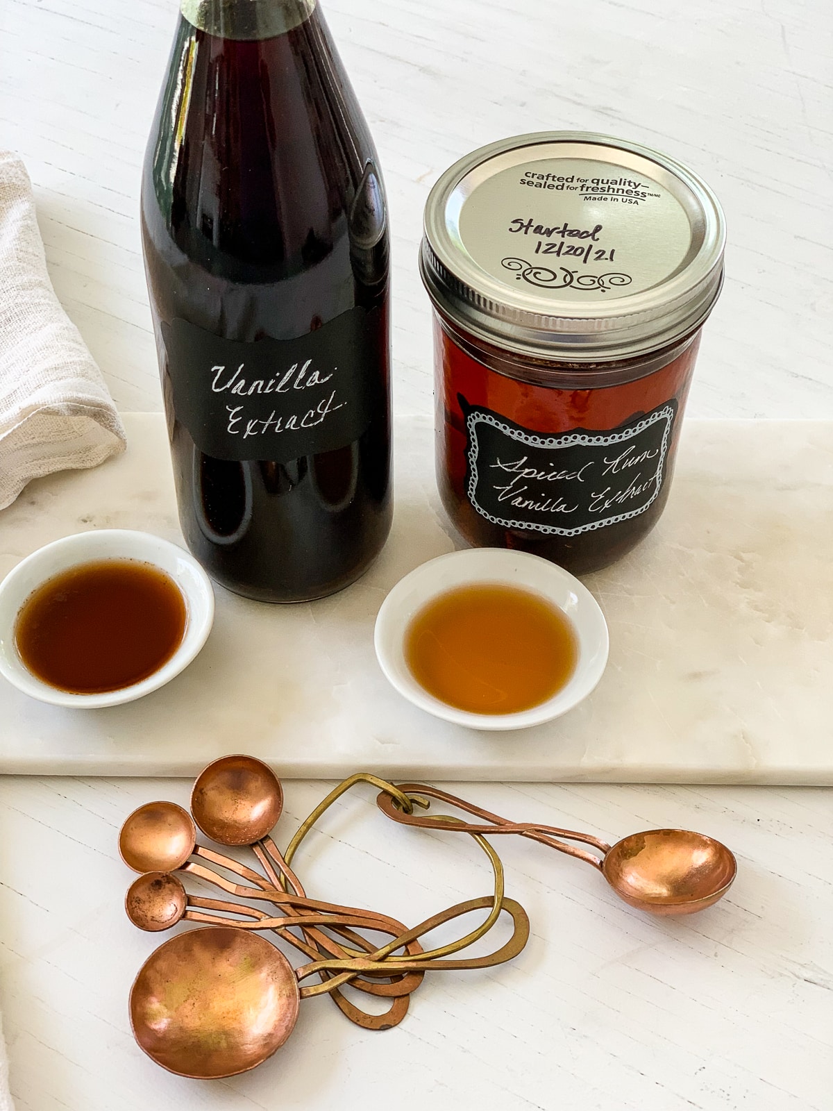 A dark bottle of vanilla extract made at home with a small jar of spiced rum extract on a kitchen counter.