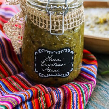 A glass jar with a clamp filled with green enchilada sauce on a colorful striped piece of cloth.