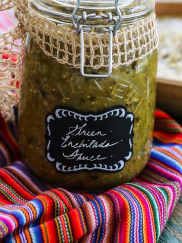 A glass jar with a clamp filled with green enchilada sauce on a colorful striped piece of cloth.