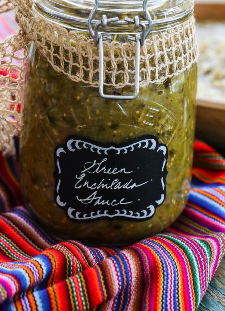 A glass jar with a clamp filled with green enchilada sauce on a colorful striped piece of cloth.