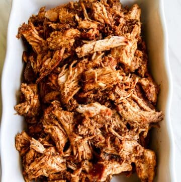 A white casserole dish with oven roasted pulled pork shredded and ready to eat in tacos or a recipe for dinner.